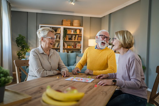 Group of senior people man and woman husband and wife friends or family play leisure board game at home have fun pensioner grandfather and grandmother spend time together with their mature daughter