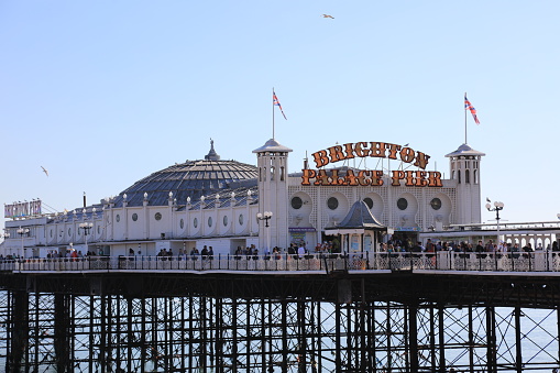Brighton, United Kingdom - April 15, 2022: Brighton Palace Pier with people sitting on the beach, East Sussex, England.