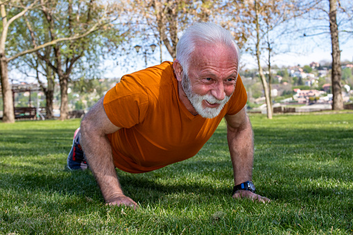 Portrait of a senior man exercising, doing push ups in the park. An elderly man in good shape and health with strong arms.