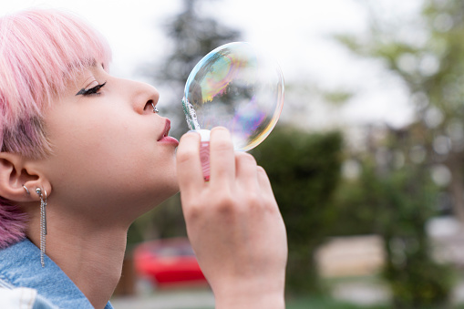 Portrait of young woman blowing bubbles in park at sunset