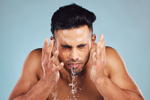 Man, water and hands in face wash for skincare, fresh clean hygiene or grooming against studio background. Young male model in beauty, wellness and washing, cleaning or cleansing for facial treatment