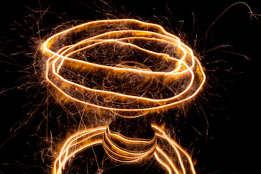 Light painting with a sparkler circling around a glass ball on a black backgtound.