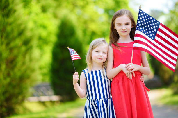 istock Two adorable little sisters holding American flags outdoors on beautiful summer day. 1483643321