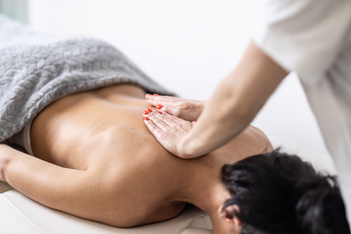 Woman masseur massages back of half-covered woman in the beautification studio.