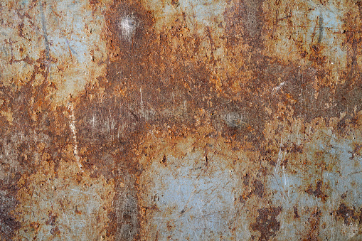 An old pitted and weathered rusty metal sheet background framed by old rusty bolts. Lots of texture with subtle abstract colors of the patina.