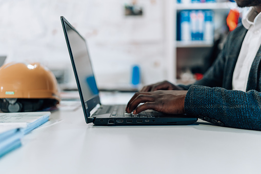 A close-up of a young African American male engineer typing on his laptop, while sitting at his desk.