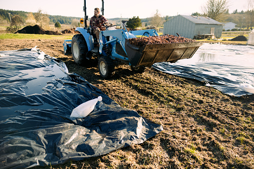 A Caucasian man works on his farm on a beautiful spring day,  using a tractor for the heavy lifting.  He prepares his soil for planting crops.  Shot in Washington state, USA.
