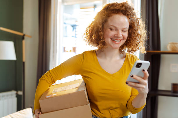 istock Happy female consumer holding cardboard boxes with online orders and using smart phone 1483656986