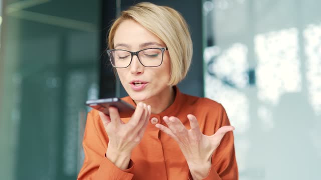 Close up of angry young blonde woman quarreling talking on smartphone while sitting at workplace at desk in modern office.