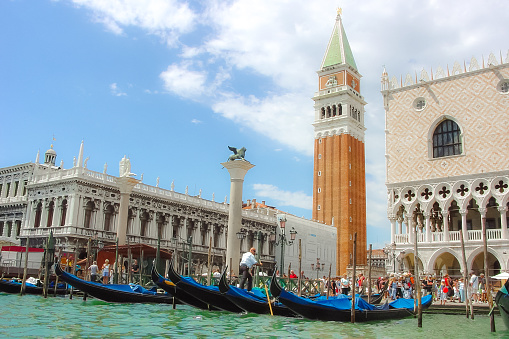 A Venetian gondolier maneuvers his gondola at the main station near St. Mark's Square with the Campanile Bell tower and Doge's Palace in view in Venice, Italy.