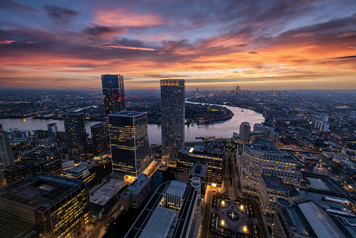Panoramic view through the modern skyscrapers of Canary Wharf of the illuminated London skyline and Thames river during dusk time, England
