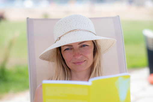 a beautiful woman with a hat is reading a book on a deck chair