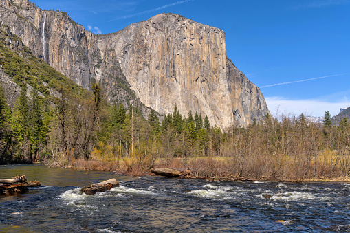 A closeup view of steep cliff wall of El Capitan towering at side of rushing Merced River on a sunny Spring evening. Yosemite National Park, California, USA.