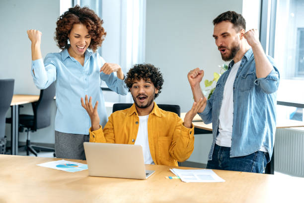 istock Joyful people of different nationalities, creative business team, working together on a project in a modern office, watching at laptop screen, rejoicing in success, good deal, profit. Success, win 1483667245