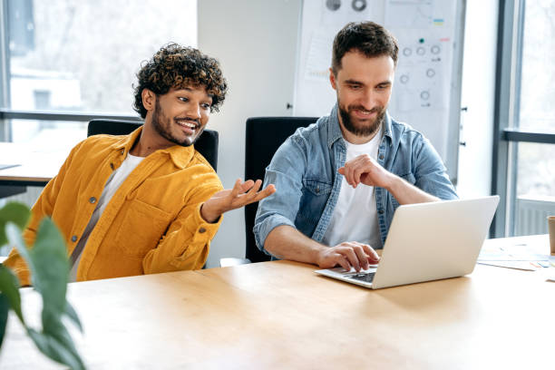 istock Positive successful colleagues, indian and caucasian men, sitting in a creative office, working on a new project, a startup, developing a strategy and an advertising campaign, analyzing risks, smiling 1483667253