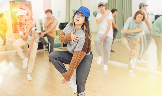 Portrait of expressive teen girl krump dancer in choreographic studio with dancing teenagers in background