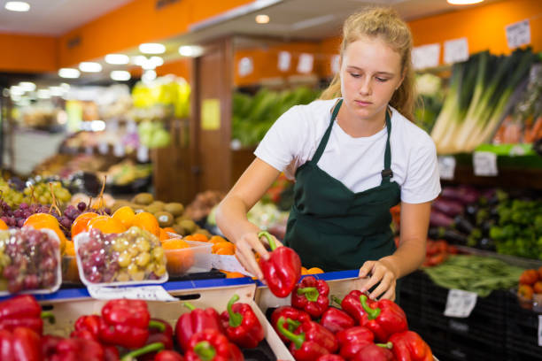 Young female seller holding pepper in grocery Young blonde salesgirl at her first job, selling bell pepper in vegetable shop 12 13 years pre adolescent child female blond hair stock pictures, royalty-free photos & images