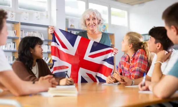 Photo of Adult female teacher discussing with children about national flag of the Great Britain at Geography lesson in library