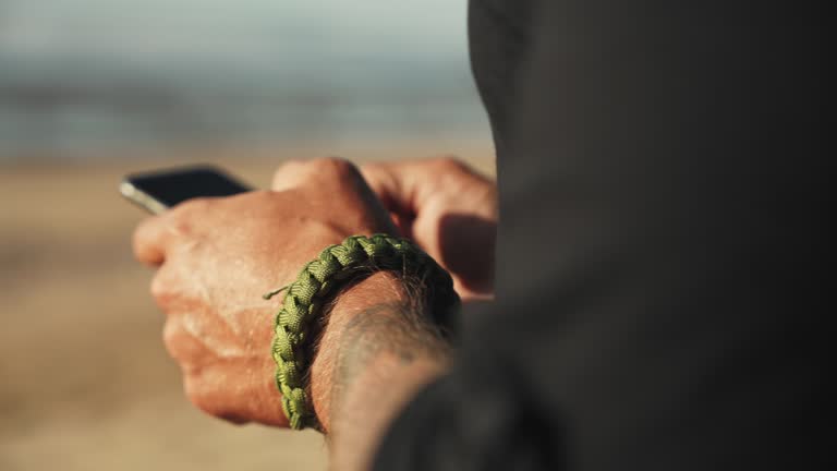 Close up hands of man with tattoos texting with smart phone on beach