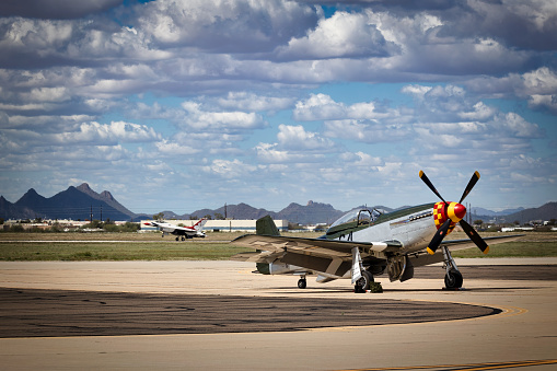 Tucson, Arizona, USA - March 24, 2023: A P-51 Mustang sits on the tarmac as an F-16 Falcon with the US Air Force Thunderbirds lands at the 2023 Thunder and Lightning Over Arizona airshow.