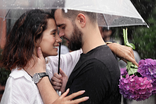 Young happy couple having fun while communicating under umbrella on rainy day in nature.