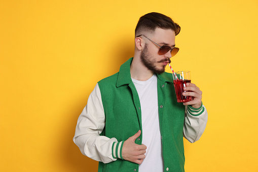 Handsome young man drinking juice on yellow background