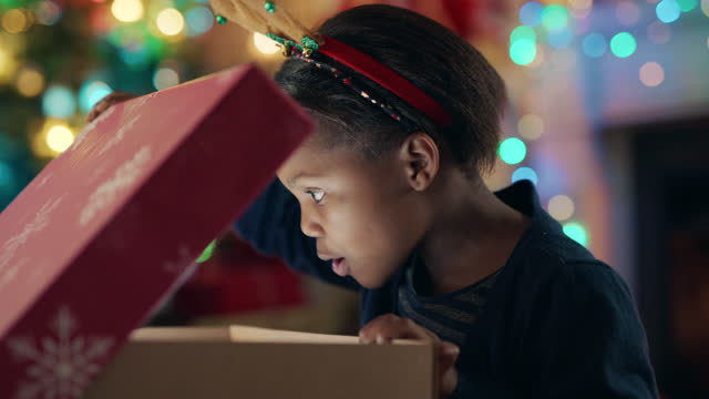 happy african american girl unwrapping christmas present looking in box with glow on face surprised child excited for special gift having fun enjoying festive holiday celebration 4k