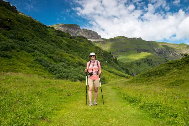 Senior woman hiking Swiss alps. Mountain-view trail from Alimendhubel to Grutschlap on a lush trail.