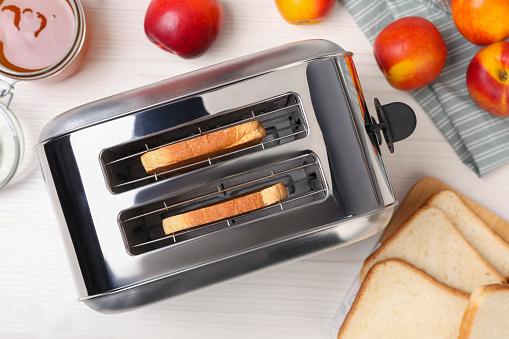 Toaster with roasted bread, nectarines and jam on white wooden table, flat lay