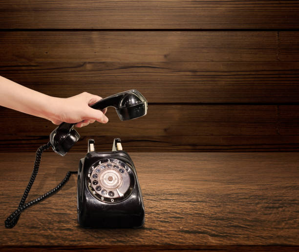 la mano di una donna raccoglie il ricevitore di un vecchio telefono. su un fondo di legno del tavolo - landline phone women close up old fashioned foto e immagini stock