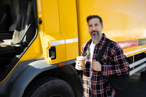 A young bearded man is sitting in the doorway of a camper van looking directly into the camera. The van is surrounded by nature in autumn colors.