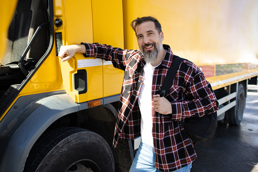 Portrait of a mature man working as a truck driver and standing by his truck