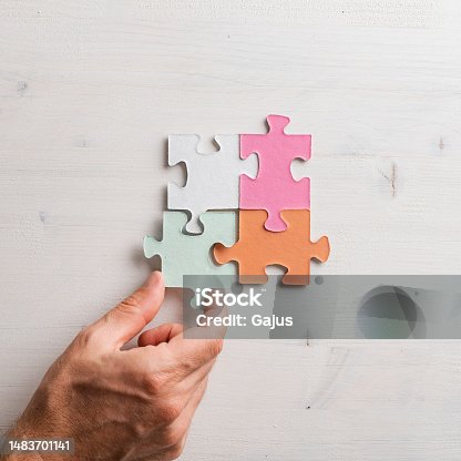 istock Top view of male hand joining four matching colorful puzzle pieces 1483701141