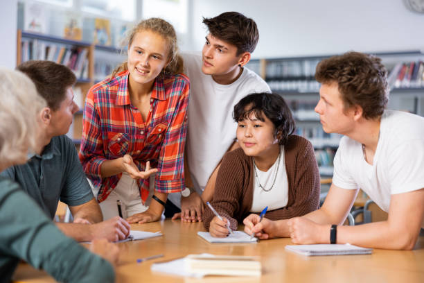 istock Positive teenage students working and discussing in groups in library 1483708545