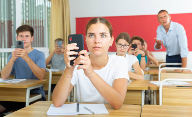 jóvenes estudiantes con teléfonos inteligentes sentados en la sala de clases - nativo digital fotografías e imágenes de stock