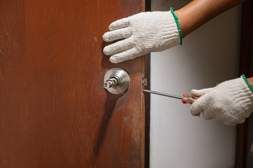Locksmith on wood door with screwdriver for repair or fix silver knob.
