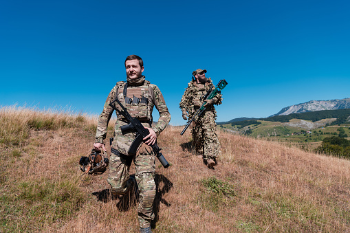 A sniper team squad of soldiers is going undercover. Sniper assistant and team leader walking and aiming in nature with yellow grass and blue sky. Tactical camouflage uniform