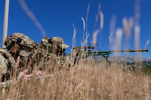 Sniper soldier assisted by an assistant to observe the area to be targeted with modern warfare tactical virtual reality goggles aerial drone military technology