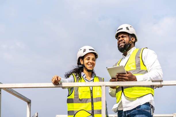 vista frontal de un hombre y una mujer afroamericanos ingenieros en uniforme discuten el uso de soporte de tabletas cerca de turbinas eólicas industria de energía ecológica, respetuoso con el medio ambiente para el futuro - alternative energy electricity wind turbine team fotografías e imágenes de stock