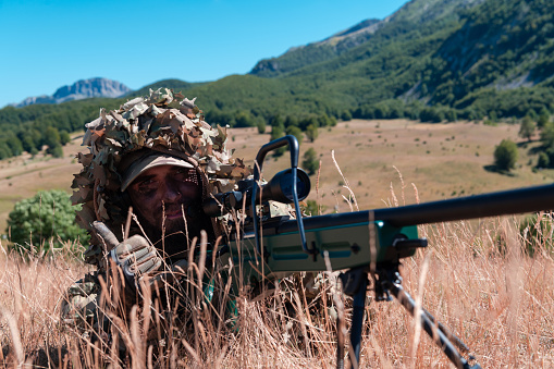 Army soldier holding sniper rifle with scope and aiming in forest. War, army, technology and people concept.