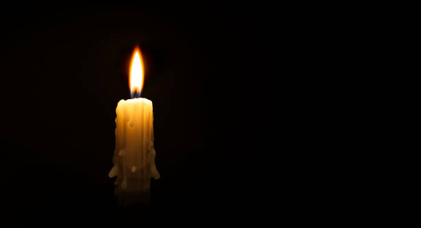Burning wax candle against a black background stock photo