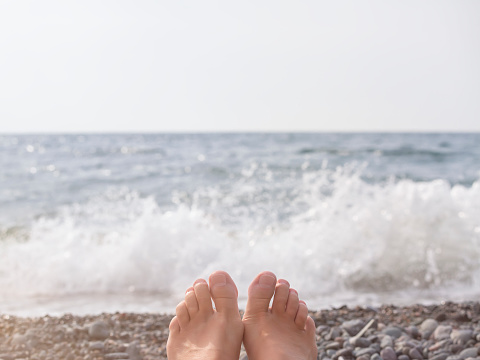 The feet of a lying woman against the background of a pebble beach and the sea