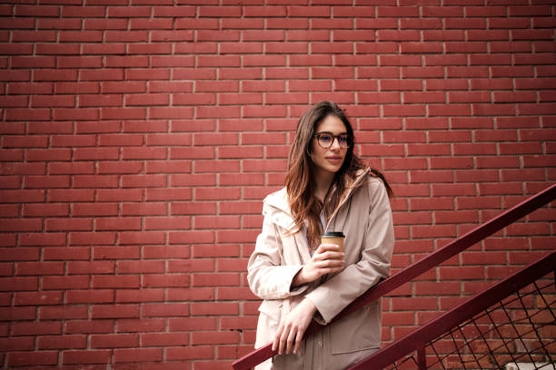 Una donna casuale in piedi all'aperto sulle scale e godersi il caffè per andare. - foto stock