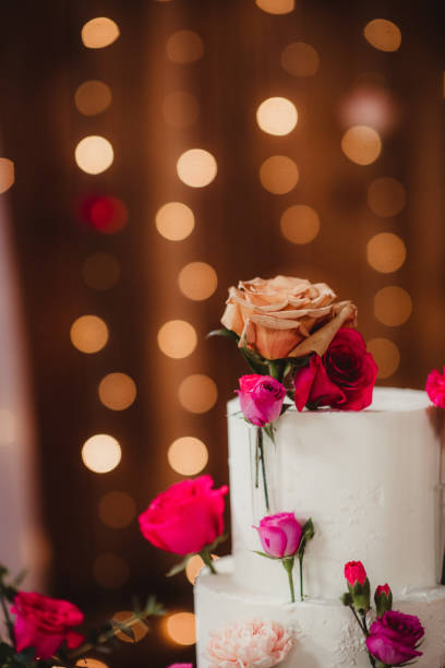 Close up of top tier of an elegant wedding cake Close up of wedding cake with string lights in the background white wedding cake red roses stock pictures, royalty-free photos & images