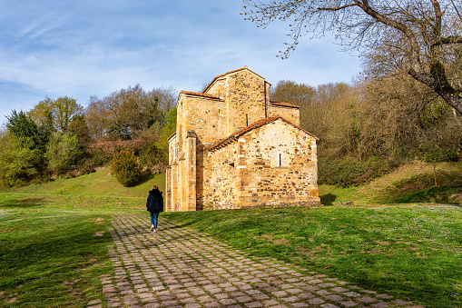Woman walking next to a very old Romanesque church located in the north of Spain, Asturias
