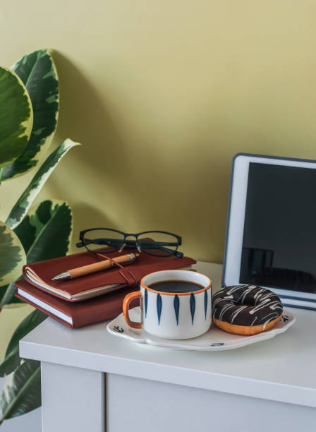 Coffee break in the home office - coffee and a donut with chocolate icing on the office desk with notebooks, tablet and stationery