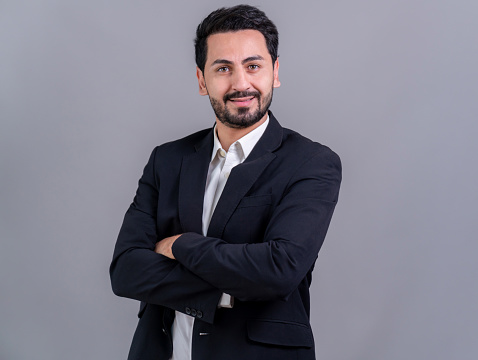Stylish businessman in black suit posing confidently on isolated background, with a happy and optimistic smile as success and professionalism for businessman. Fervent