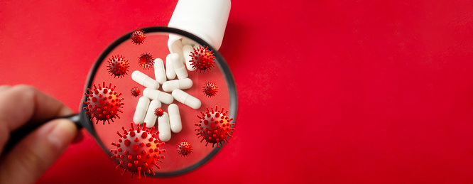 Pills through a magnifying glass, a flying virus on a red background. Medicine concept.