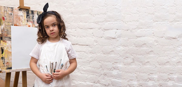 Adorable kid holding paint brushes at the art studio. Painting fine art classes.