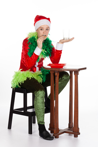 Full portrait of young girl wearing red santa clause hat like grinch nonplussed with empty milk, isolated on white background. Human emotion facial and body expression